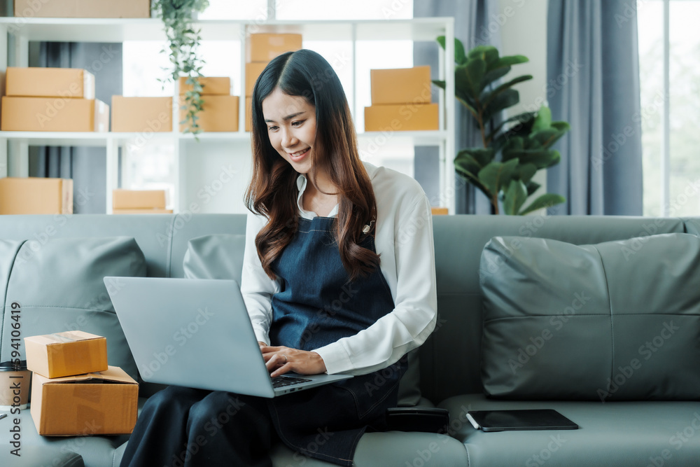 Using Laptop computer, Young pretty Asian female influencer small businesses SME owners female entrepreneurs working on receipt box and check online orders, sitting on sofa of home online business. Using Laptop computer, Young pretty Asian female influencer small businesses SME owners female entrepreneurs working on receipt box and check online orders, sitting on sofa of home online business.