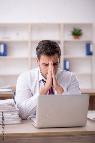 Young male employee and too much work at workplace