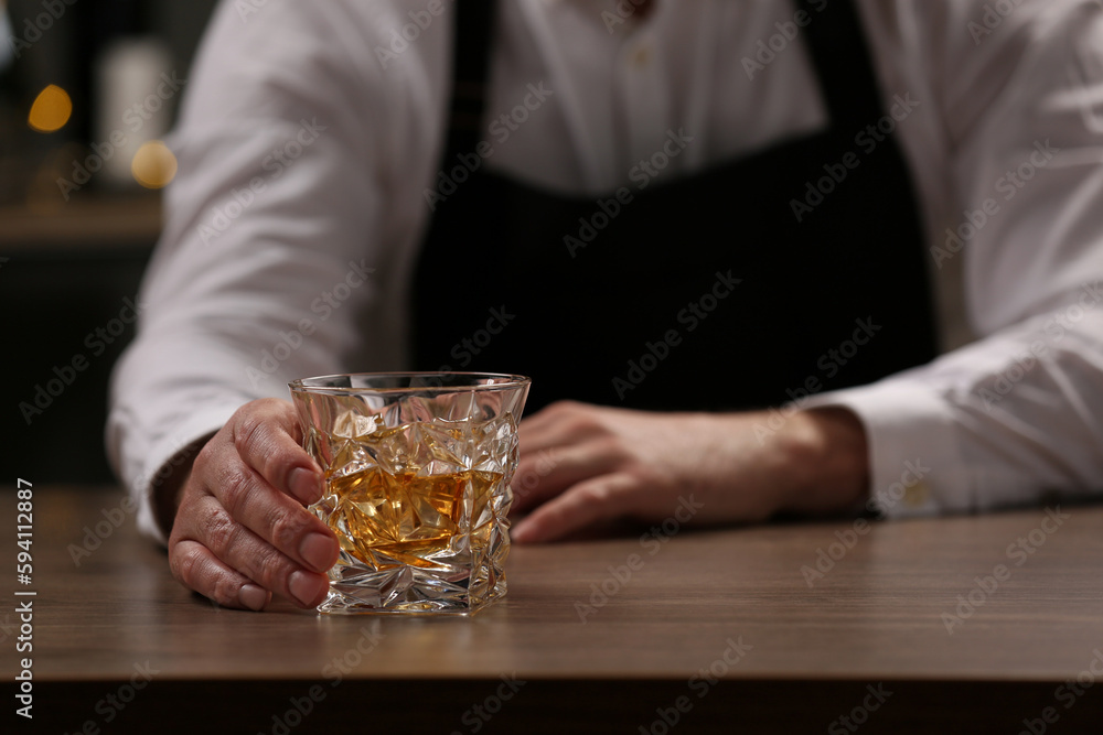 Bartender with glass of whiskey at bar counter indoors, closeup