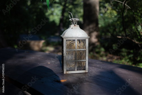 A beautiful decoration in the form of a large lantern and candlestick stands on a table illuminated by the morning sun on a wonderful summer day.morning. The concept of aesthetic relaxation in nature. © Anton