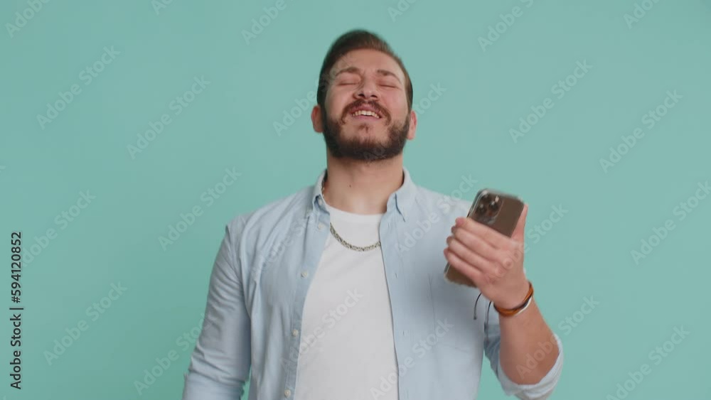 Lebanese man use mobile cell phone typing browsing, loses becoming surprised sudden lottery results, bad fortune, loss, fail. Handsome arabian guy isolated alone on blue studio wall background indoors Lebanese man use mobile cell phone typing browsing, loses becoming surprised sudden lottery results, bad fortune, loss, fail. Handsome arabian guy isolated alone on blue studio wall background indoors