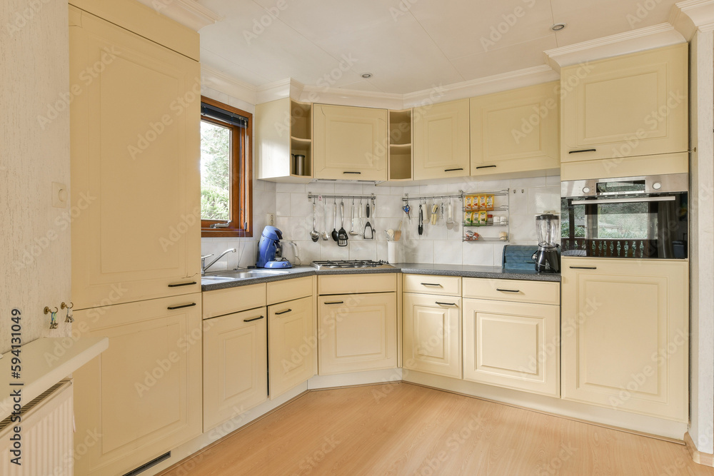Fototapeta premium a kitchen with white cabinets and light wood flooring in the middle of the room, looking into the dining area