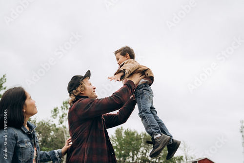 Side view of mam, dad and son. Father throwing up the son, playing together. Happy family smiling, laughing, Concept of family relations.
