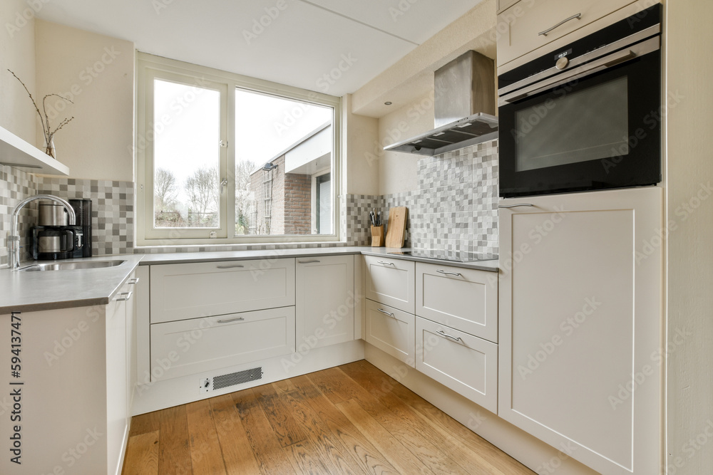 a kitchen with wood flooring and white cupboards on either side of the window, there is an oven in the corner a kitchen with wood flooring and white cupboards on either side of the window, there is an oven in the corner