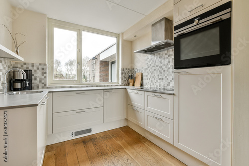 a kitchen with wood flooring and white cupboards on either side of the window  there is an oven in the corner