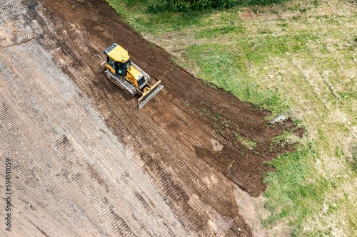 yellow tracked bulldozer performs earthworks on construction site. aerial view from flying drone.