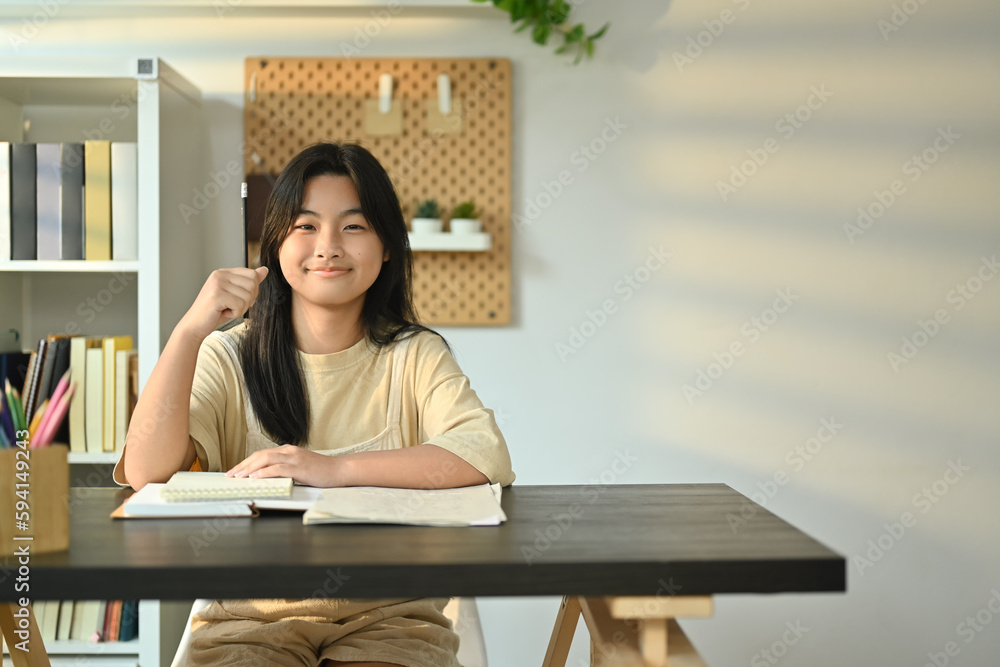 Cute teenager girl with a lovely engaging smile sitting at a desk in living room. Homeschooling, learning, self education Cute teenager girl with a lovely engaging smile sitting at a desk in living room. Homeschooling, learning, self education