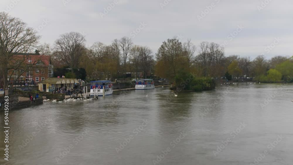 View of the River Thames from the Eton Bridge. The river is calm and serene, with ducks, boats and swans swimming. Surrounding area is lush and green. View of the River Thames from the Eton Bridge. The river is calm and serene, with ducks, boats and swans swimming. Surrounding area is lush and green.