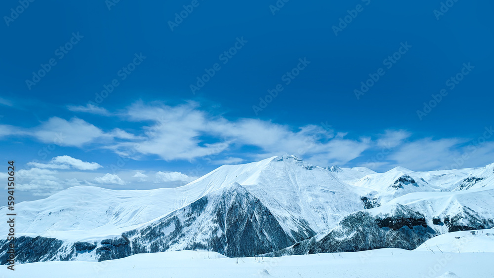 Mountains and hills covered with snow under the sun and bright blue sky in Gudauri, Georgia
