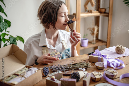 Woman in an apron is packing natural lavender soap and decorating it with lavender flowers. Concept of natural soap and handmade gifts