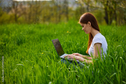 a woman works remotely at a laptop being outdoors in tall grass