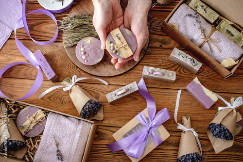 Fragrant lavender bouquets wrapped in craft paper with ribbon, natural soap and gift boxes on a wooden table. Concept of packing handmade presents