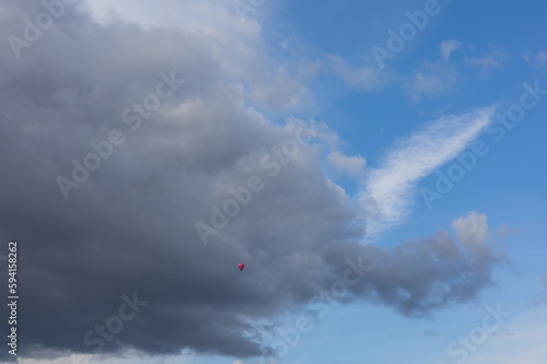 Pink flying balloon on blue sky with clouds.