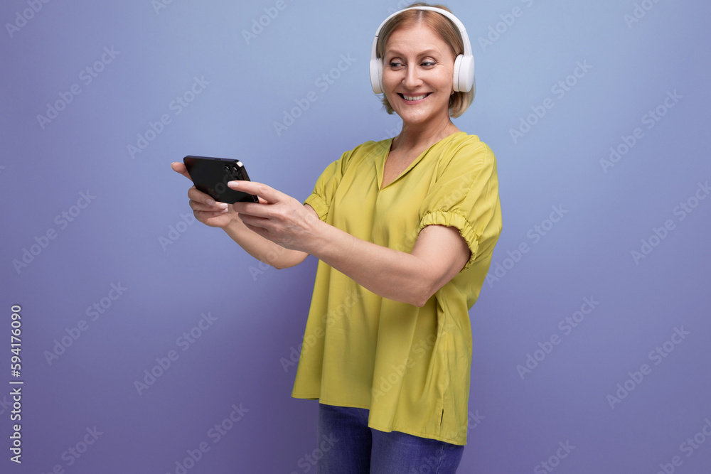 joyful blond mature woman watching video on smartphone using headphones joyful blond mature woman watching video on smartphone using headphones