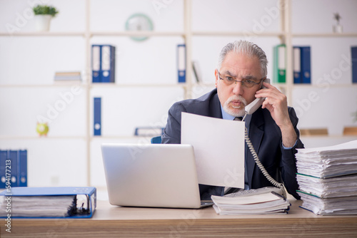 Old male employee speaking by phone in the office