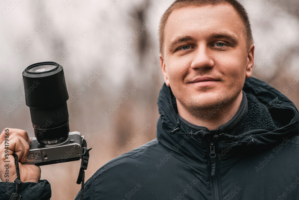 Man holds the DSLR camera with one hand while looking into the camera.
