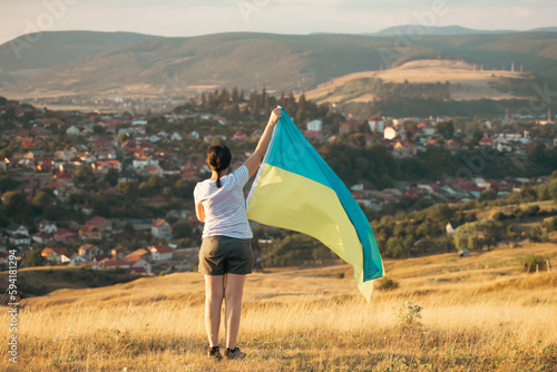 Woman holding a yellow and blue flag of Ukraine on a background of a small city.