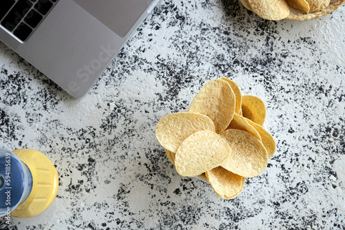 Top view of white bowls with potato chips and a laptop on a beautiful decorative table.