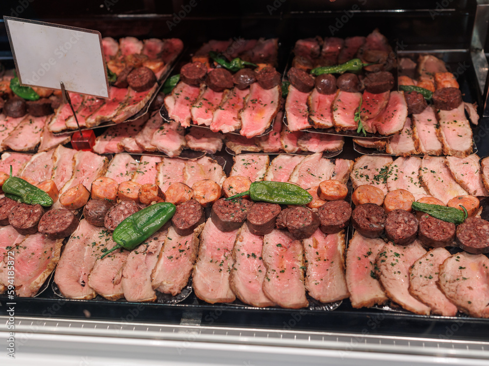 Slices of Cooked Meat, Slices of Sausages and Green Peppers displayed on a Retail Counter