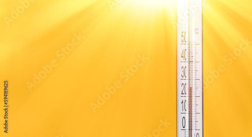 Outdoor thermometer with mark of twenty-five degrees Celsius against yellow background under sunlight.