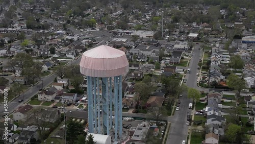 An aerial view of a water tower in Elmont, New York under a tarp on a cloudy day. The tower is being repainted, after years of rust and decay. The camera slowly dolly in until down over the tower. photo