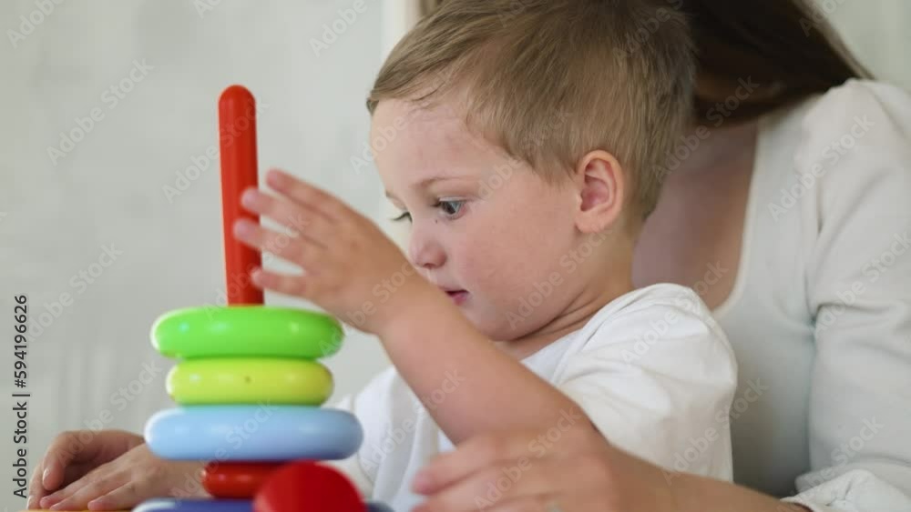 Happy family. Child with nanny at table collect pyramid. Mom and son play with colored pyramid at home. Boy is sitting at table in kindergarten. Parent teaches kid in the game. Education Kindergarten