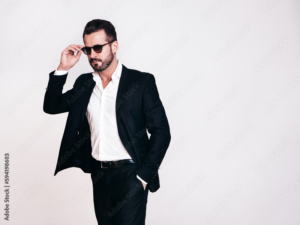 Portrait of handsome confident stylish hipster lambersexual model. Sexy modern man dressed in black elegant suit. Fashion male posing in studio, isolated on white. Sunglasses Portrait of handsome confident stylish hipster lambersexual model. Sexy modern man dressed in black elegant suit. Fashion male posing in studio, isolated on white. Sunglasses