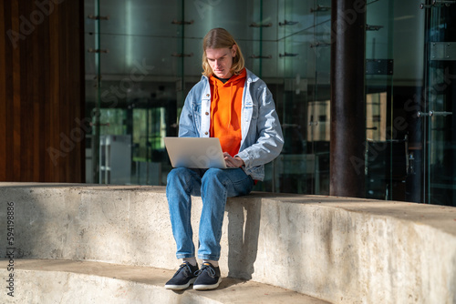 Focused man student studying working on research project sitting on cement steps near university building. Guy learning, writing educational tasks, doing homework. Education, give knowledges concept. © DimaBerlin