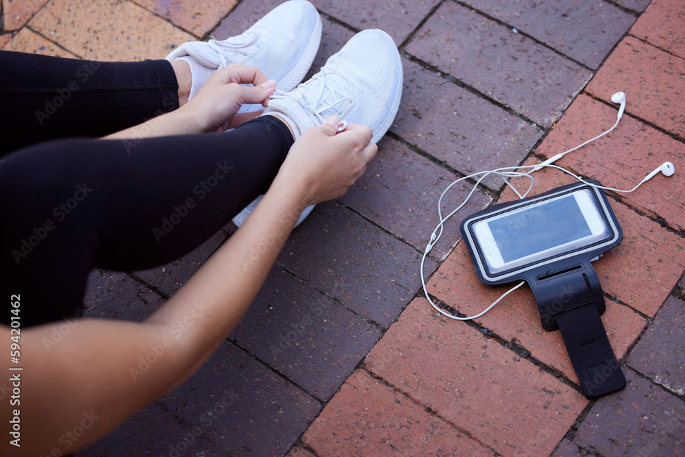 Phone, fitness and footwear from above with a woman athlete sitting on the ground to tie laces. Exercise, music and getting ready for running with a female sports person outdoor for cardio training