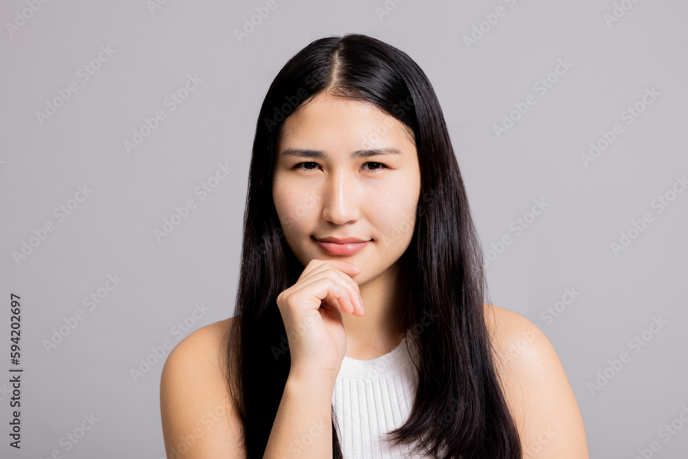 Curious thoughtful young happy asian woman with black dark long hair holding hand near face natural make up skincare welness on greu background isolated. Curious thoughtful young happy asian woman with black dark long hair holding hand near face natural make up skincare welness on greu background isolated.