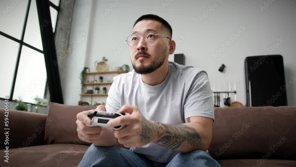 30s Man Plays Video Game. Korean man holding game joystick controller sitting on couch at home. 30s Man Plays Video Game. Korean man holding game joystick controller sitting on couch at home.