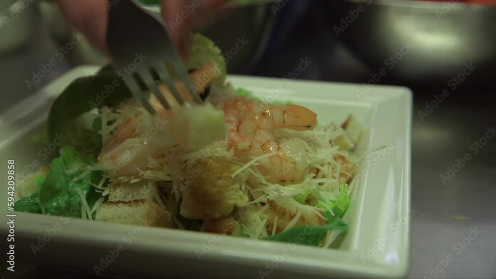 dolly macro shot of shrimp being added to the caesar salad, female cook hands with fork working quickly dolly macro shot of shrimp being added to the caesar salad, female cook hands with fork working quickly