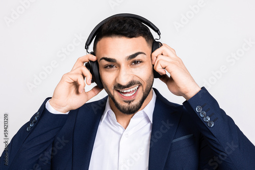 Happy turkish man in suit buisnessman in headphones arphones standing over grey background in studio isolated looking at camera recieving call call centre time work. photo