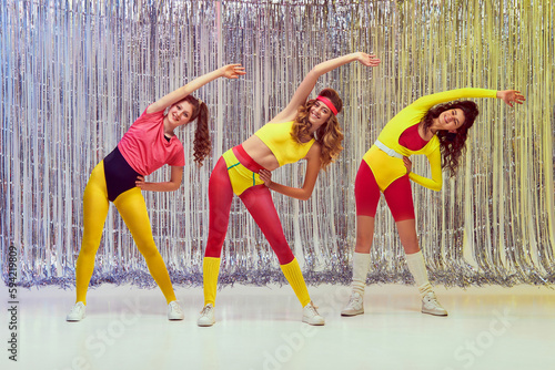 Fototapeta Naklejka Na Ścianę i Meble -  Sportive, active, young women in colorful, comfortable sportswear training, doing stretching and aerobics exercises. Slim fit body. Concept of retro fitness, sport, 80s fashion, beauty, health