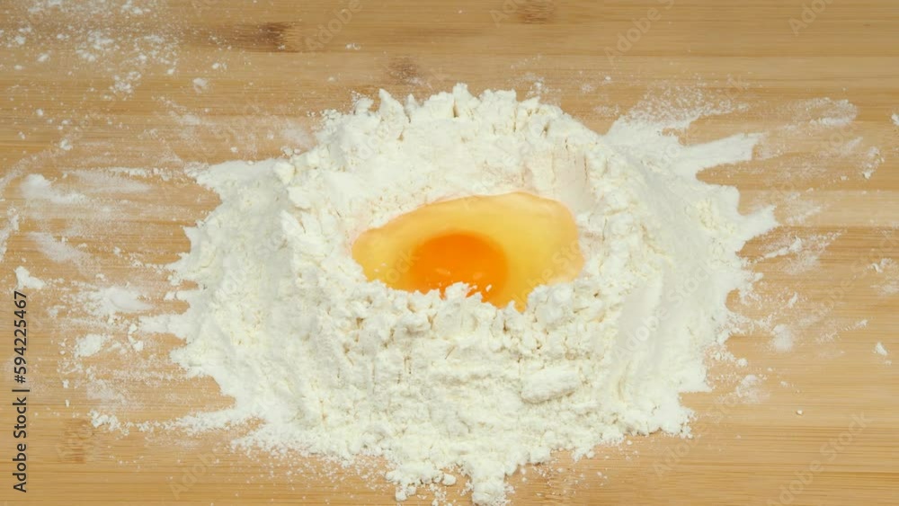 Falling eggs into the flour. Hands cracking a raw egg over the flour. The process of breaking eggs. Baker making the dough. Falling eggs into the flour. Hands cracking a raw egg over the flour. The process of breaking eggs. Baker making the dough.