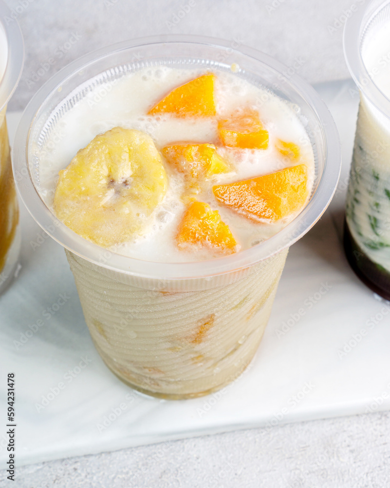 Kolak pisang ubi, kolak biji salak is Indonesian Dessert during Ramadhan made from banana, sweet potato cooked with coconut Milk, palm Sugar. Serving in plastic glass, white background.