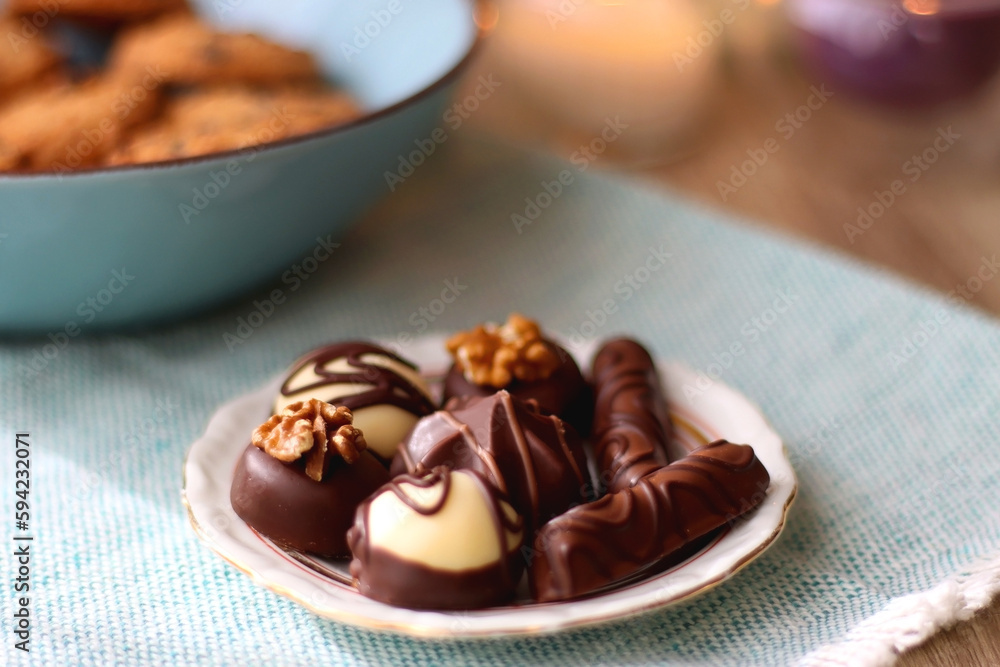 Plate of chocolate pralines, bowl of cookies, cups of tea, glasses of juice and lit candles on the table. Selective focus. Plate of chocolate pralines, bowl of cookies, cups of tea, glasses of juice and lit candles on the table. Selective focus.