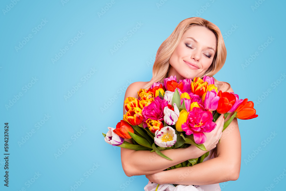 Portrait with copy space, empty place of pretty cute lovely woman with close eyes having big colorful aromatic bouquet of tulips in hands isolated on pink background