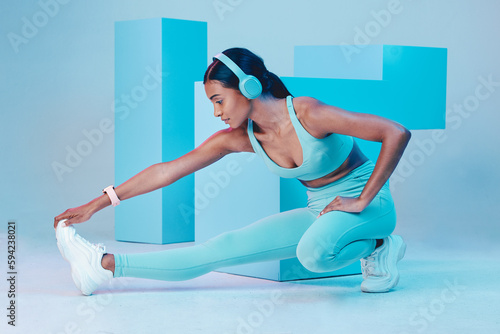 Fototapeta Naklejka Na Ścianę i Meble -  Headphones, stretching and fitness woman isolated on blue background for workout, training or exercise music. Legs, sports and biracial person listening to audio, muscle health and wellness in studio
