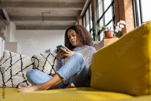 African American Student on Sofa looking at Smartphone in loft apartment photo