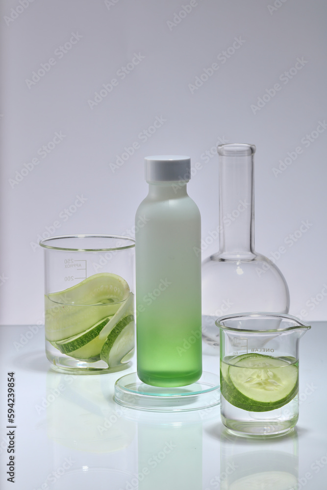 Against a white background, an unbranded bottle is decorated with beakers and a flat-bottom florence flask. Cucumber (Cucumis sativus) can be highly beneficial for your skin Against a white background, an unbranded bottle is decorated with beakers and a flat-bottom florence flask. Cucumber (Cucumis sativus) can be highly beneficial for your skin