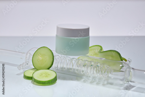 An unlabeled jar placed on a glass condenser with some Cucumber slices arranged around. The natural astringent properties of Cucumber (Cucumis sativus) work to reduce puffiness photo