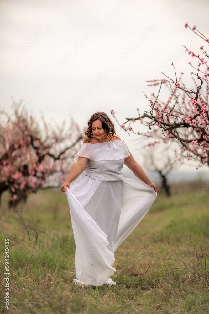 Woman peach blossom. Happy woman in white dress walking in the garden of blossoming peach trees in spring