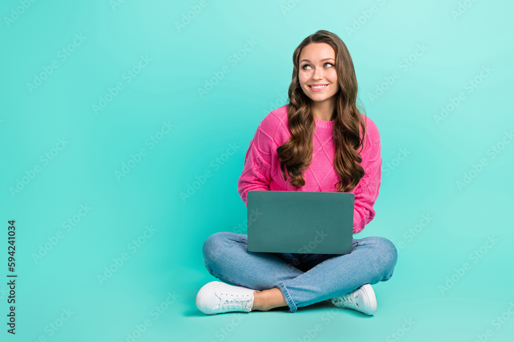 Full length photo of gorgeous positive girl sitting floor promoting netbook device shop empty space isolated on cyan color background Full length photo of gorgeous positive girl sitting floor promoting netbook device shop empty space isolated on cyan color background