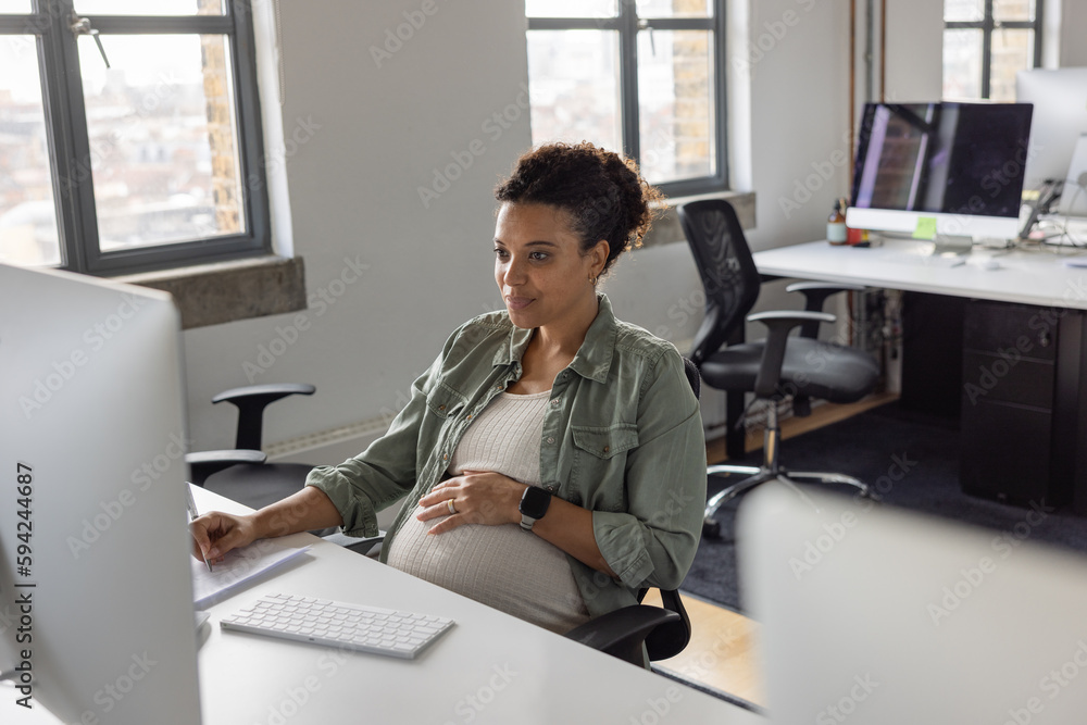 Pregnant businesswoman working at a desktop computer in an office smiling Pregnant businesswoman working at a desktop computer in an office smiling