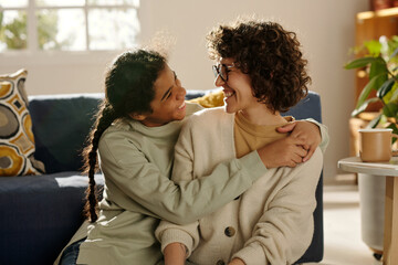 African American happy teenage girl embracing her foster mom while they spending time together at home