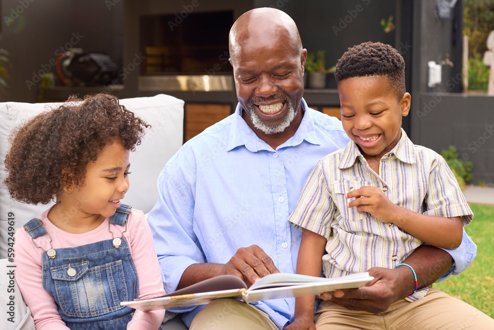 Fototapeta premium Smiling Grandfather Reading Book With Grandchildren In Garden Together