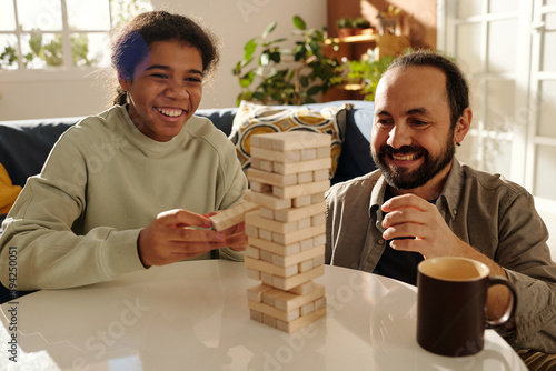Happy African American teenage girl playing jenga with her foster dad at table in the living room