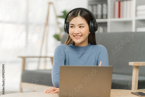 Beautiful smiling young woman in headphones chatting via laptop computer video call at home