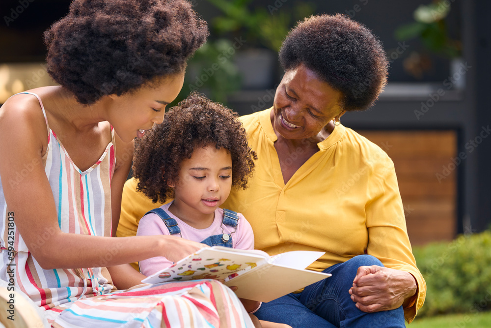 Smiling Multi-Generation Female Family Reading Book In Garden Together Smiling Multi-Generation Female Family Reading Book In Garden Together